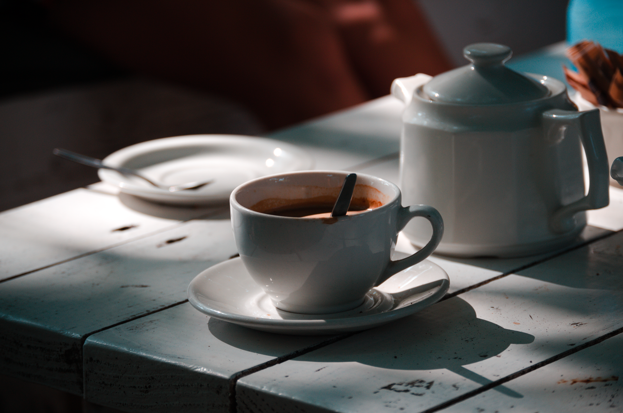 White coffee cup and pot on sun-dappled table, creating a cozy atmosphere.