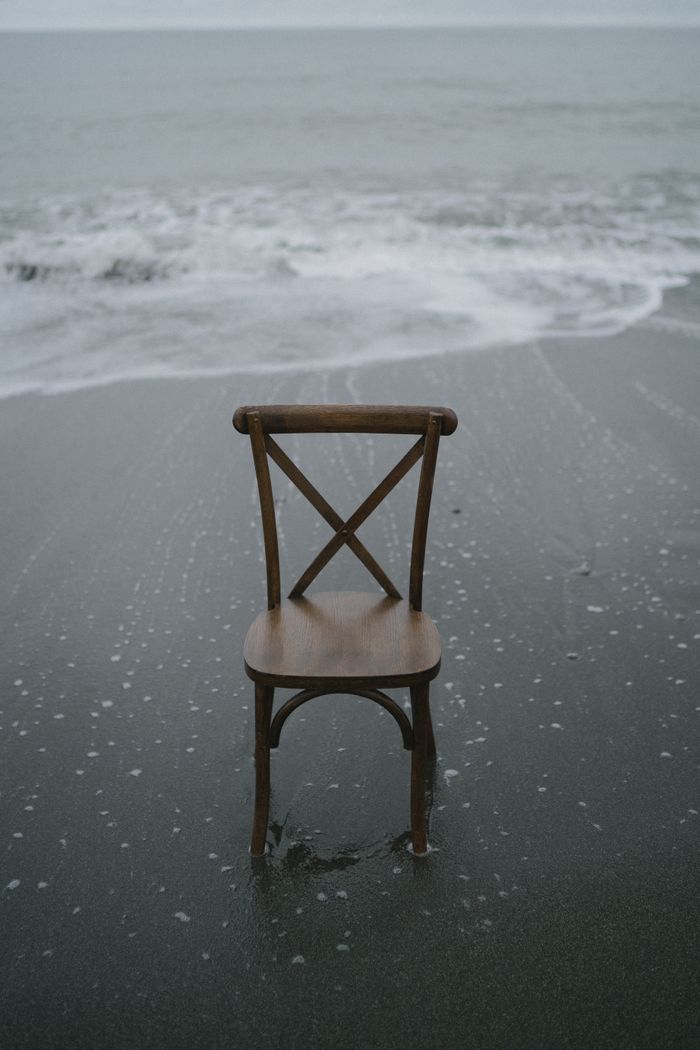 A single wooden chair facing the ocean waves on a sandy beach.